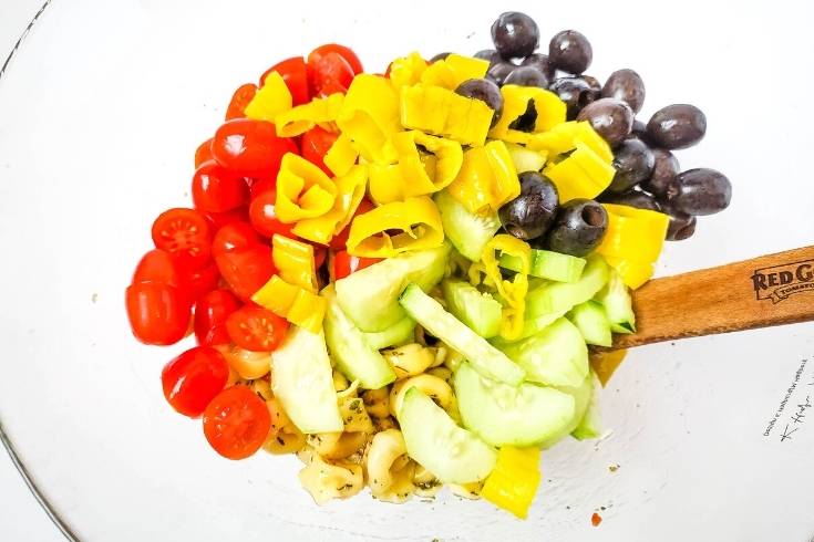 mix ingredients for italian tortellini pasta salad together in bowl