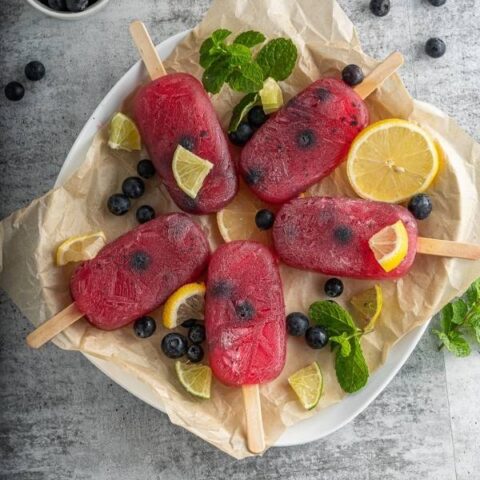 blueberry lemon popsicles on a plate with fresh fruit slices
